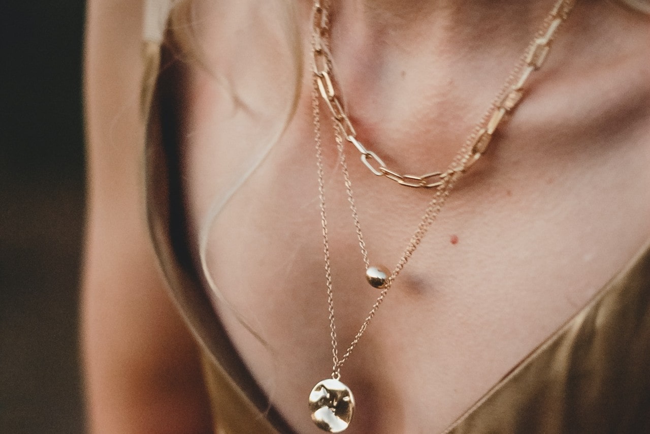 a close up image of a woman’s neckline adorned with three gold necklaces of varying lengths.