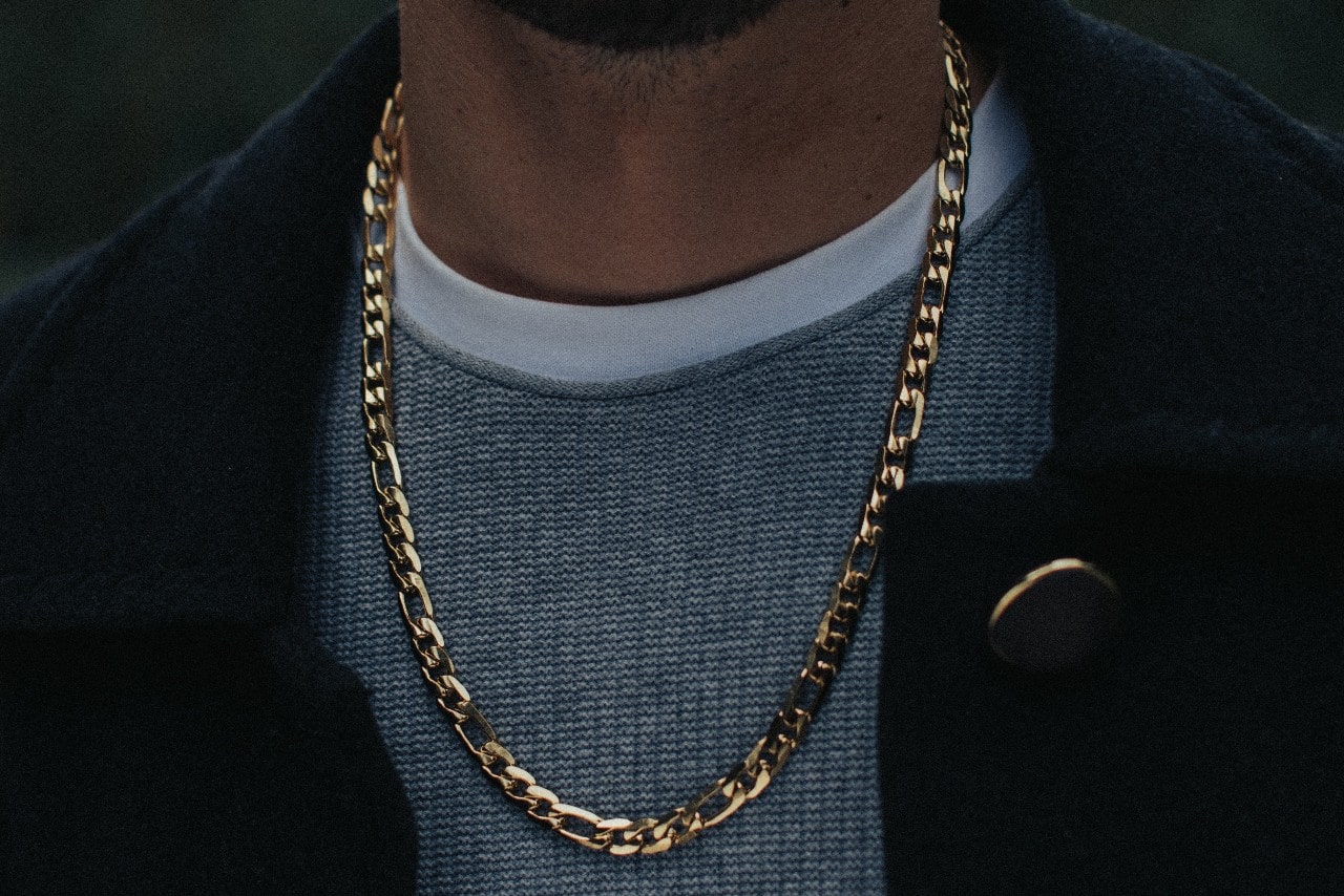 close up image of a man wearing a sweater and a yellow gold chain necklace