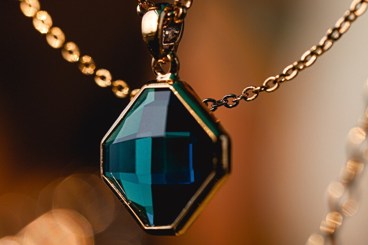 close up image of a gold necklace featuring a prominent blue gemstone pendant