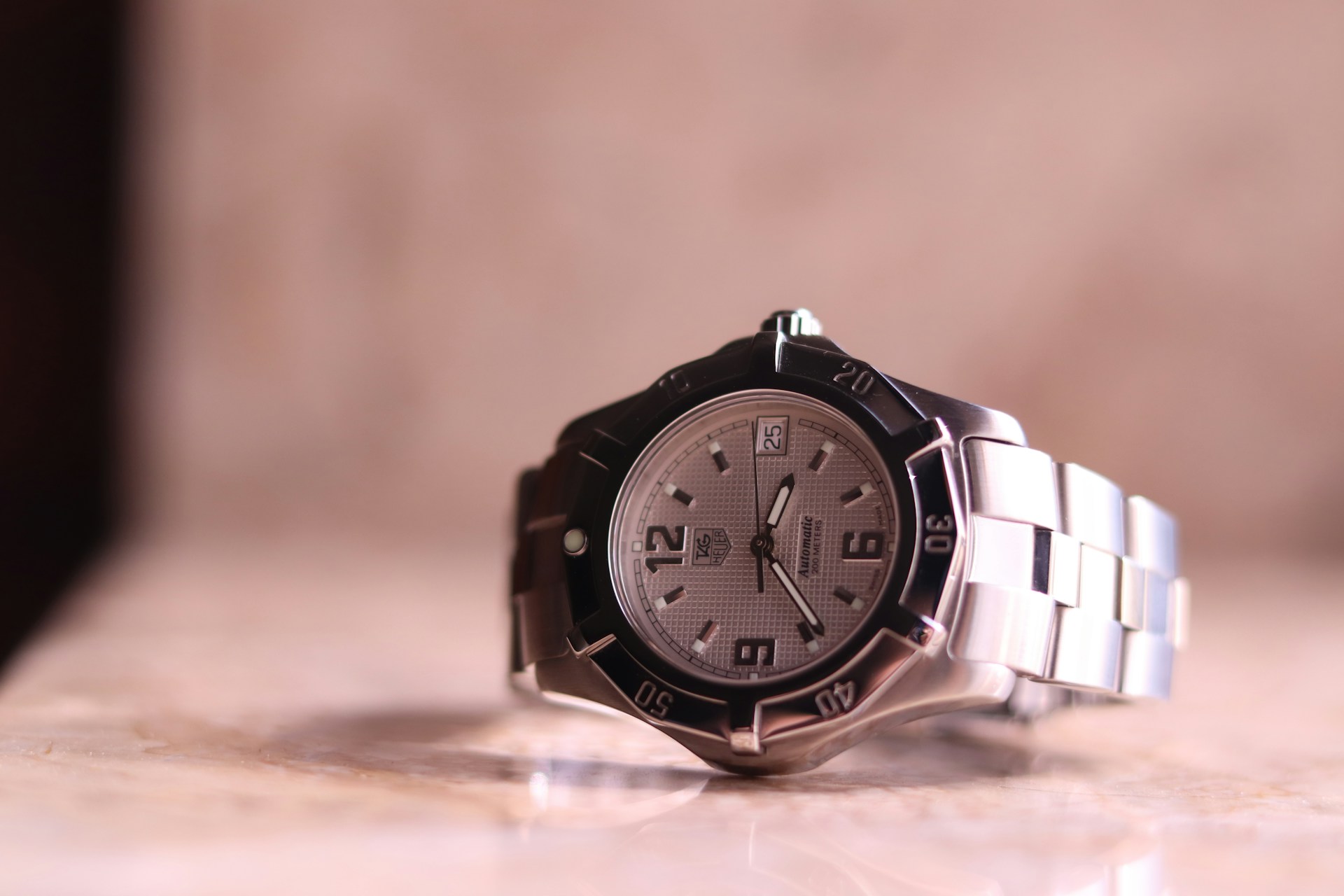 A close-up of a TAG Heuer watch on a tan marble backdrop.