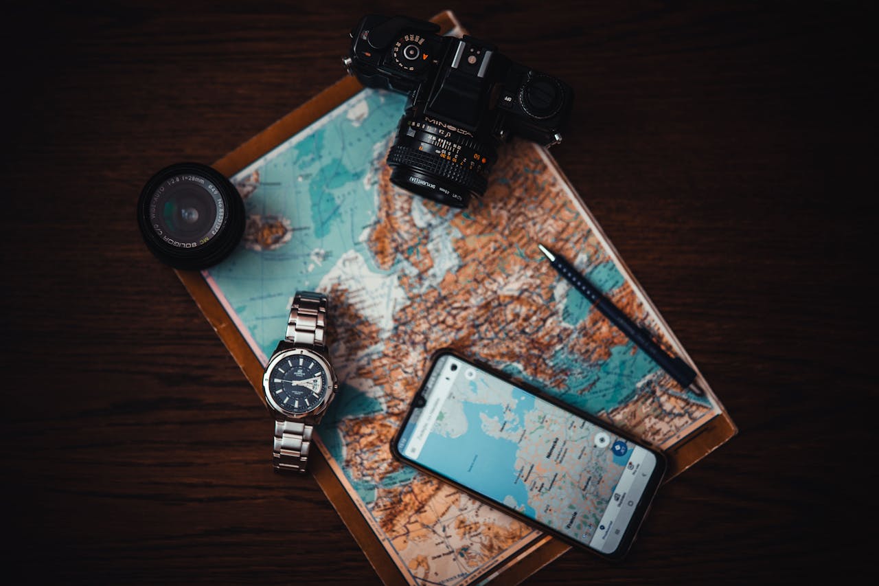 A camera, camera lens, luxury watch, phone, and pen all laying on top of a map.