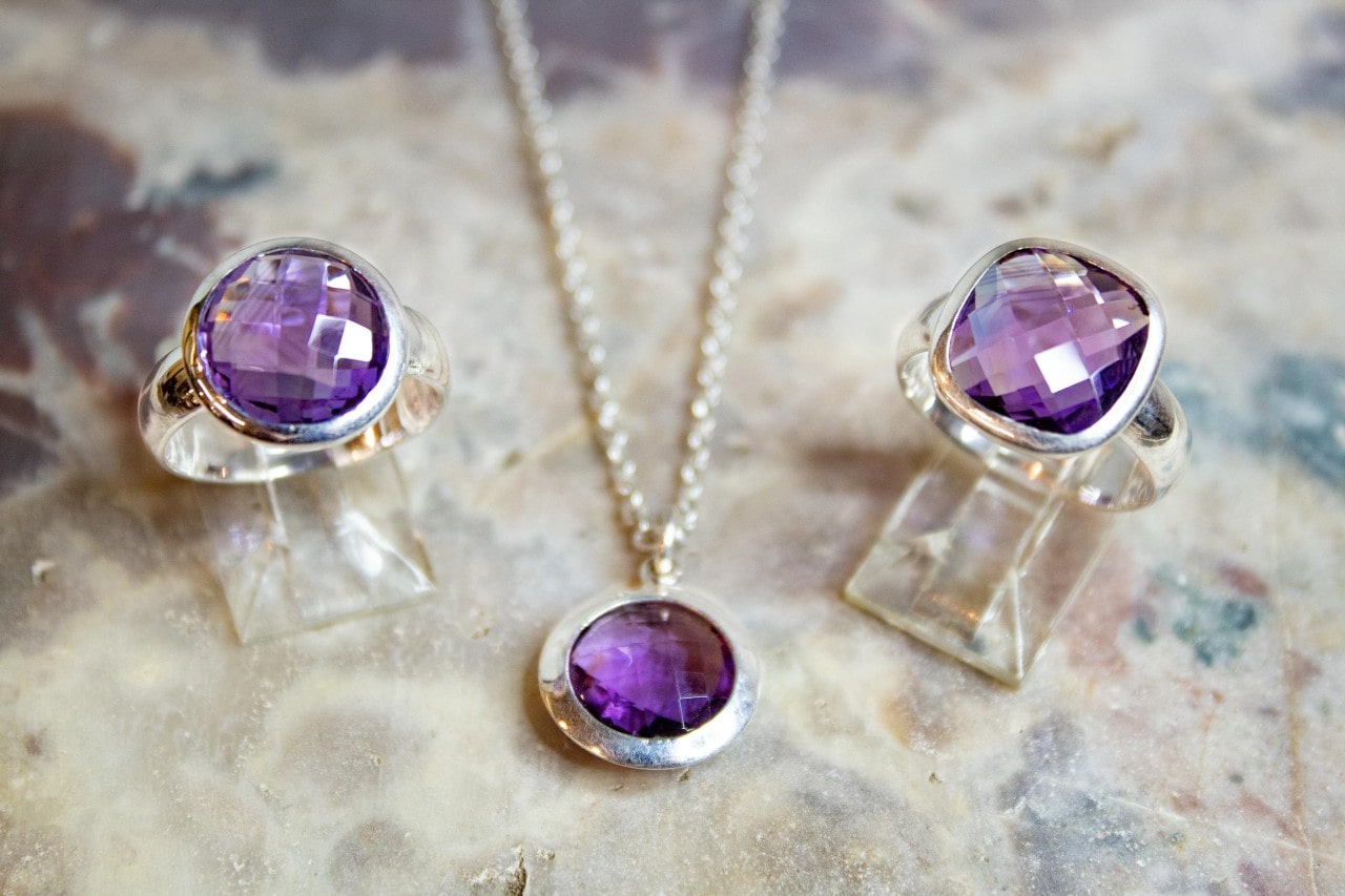 A close-up of three matching pieces of white gold and amethyst jewelry on a granite surface.