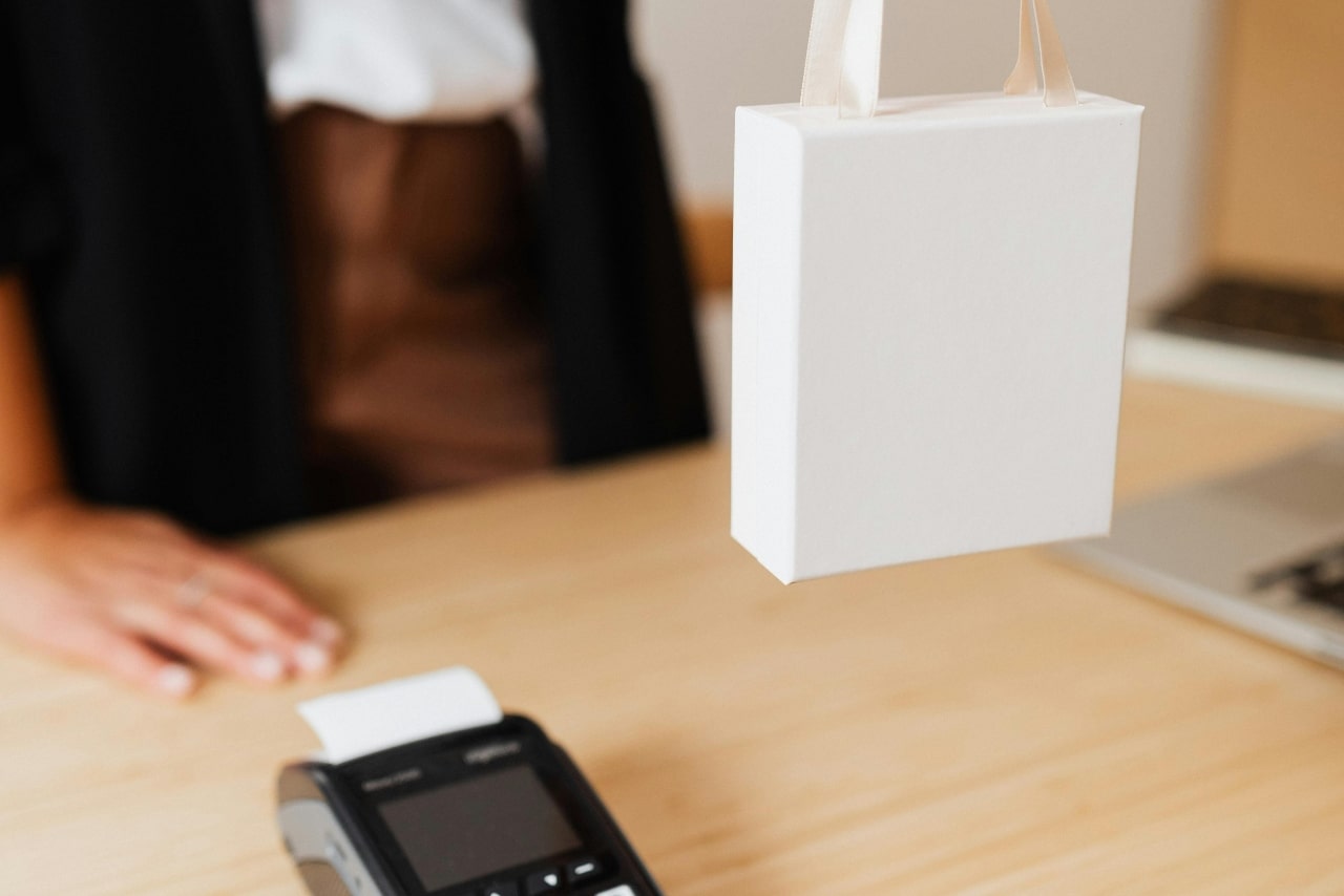 A close-up of a small white shopping bag being passed over a store counter.