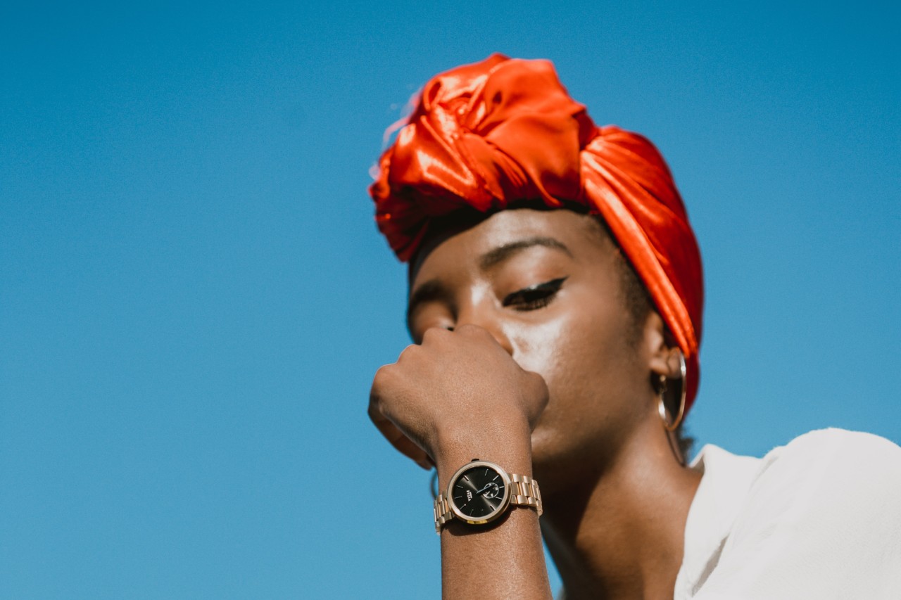 A woman wearing a red head covering shows off her gold watch.