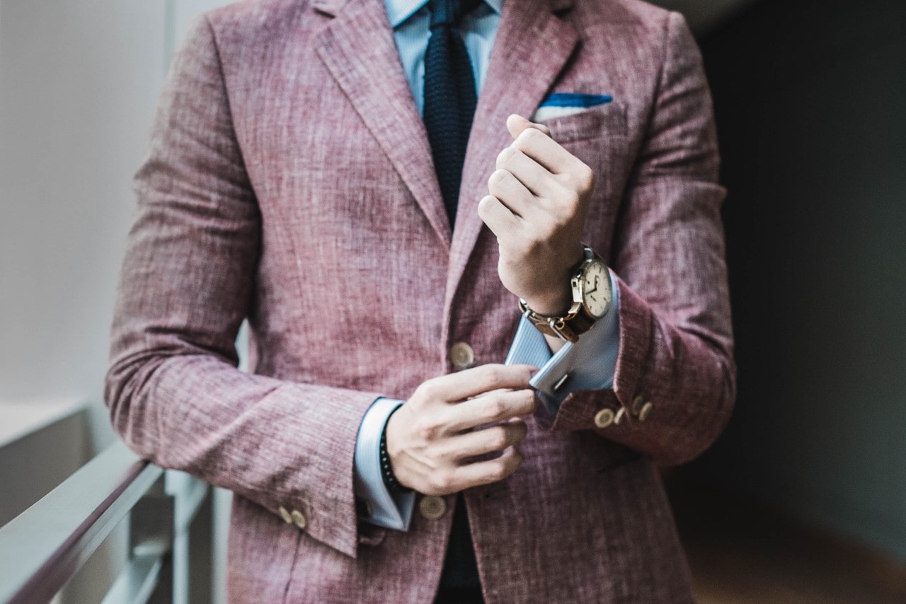 Close-up of a man adjusting cufflink on his light blue shirt sleeve, while wearing a brown leather strap watch.