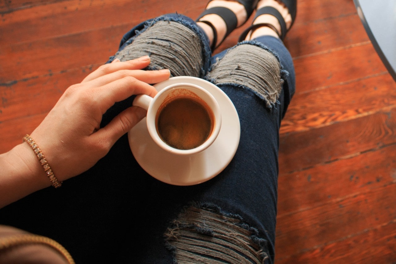 A woman wearing a tennis bracelet sips a latte on the floor.