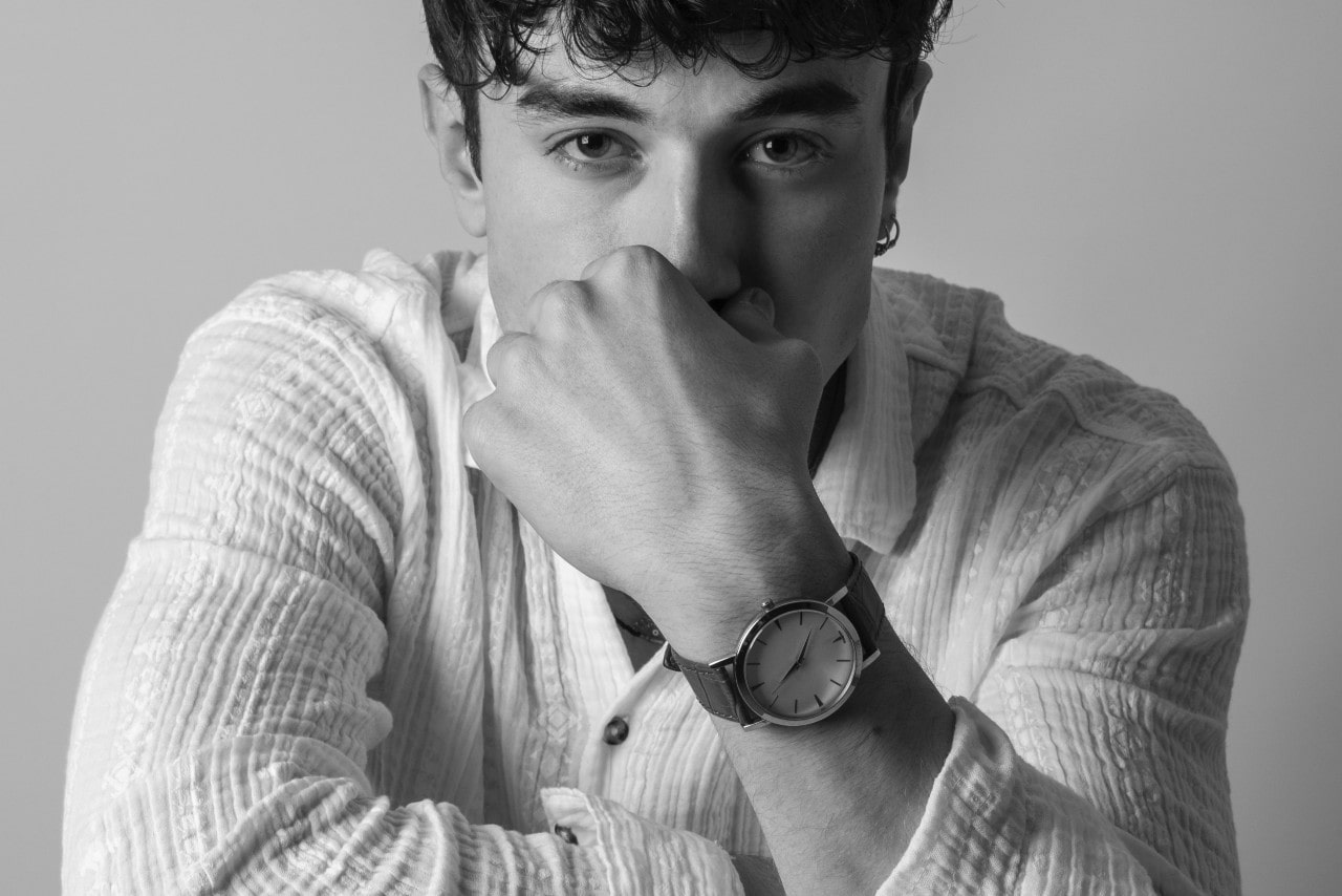 A black and white image of a man staring into the camera, resting his hand on his face to showcase his watch.