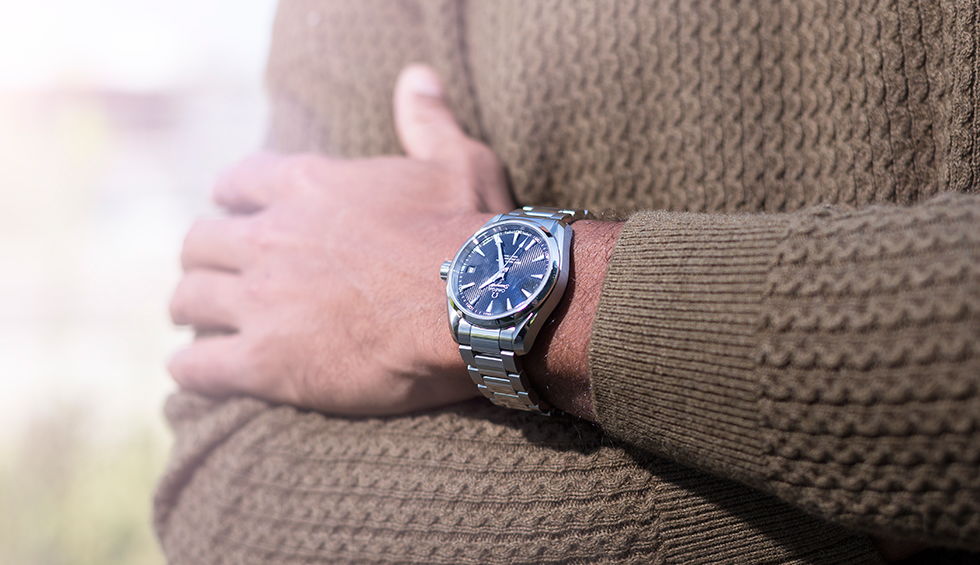A close-up shot of a man&rsquo;s wrist, adorning an Omega Seamaster watch with deep blue dial and metallic bracelet.