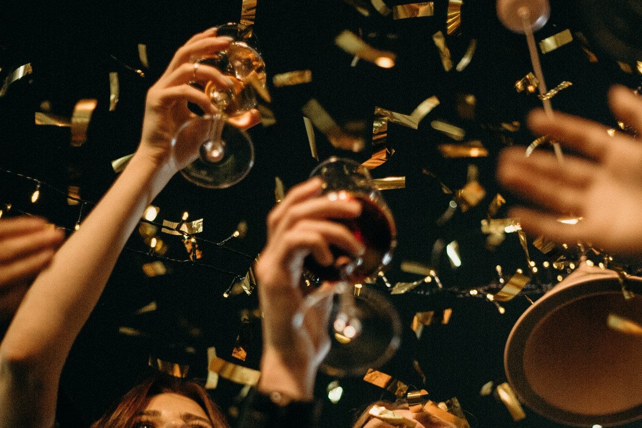 A low-angle view of people’s hands as they toast the new year as golden confetti falls.