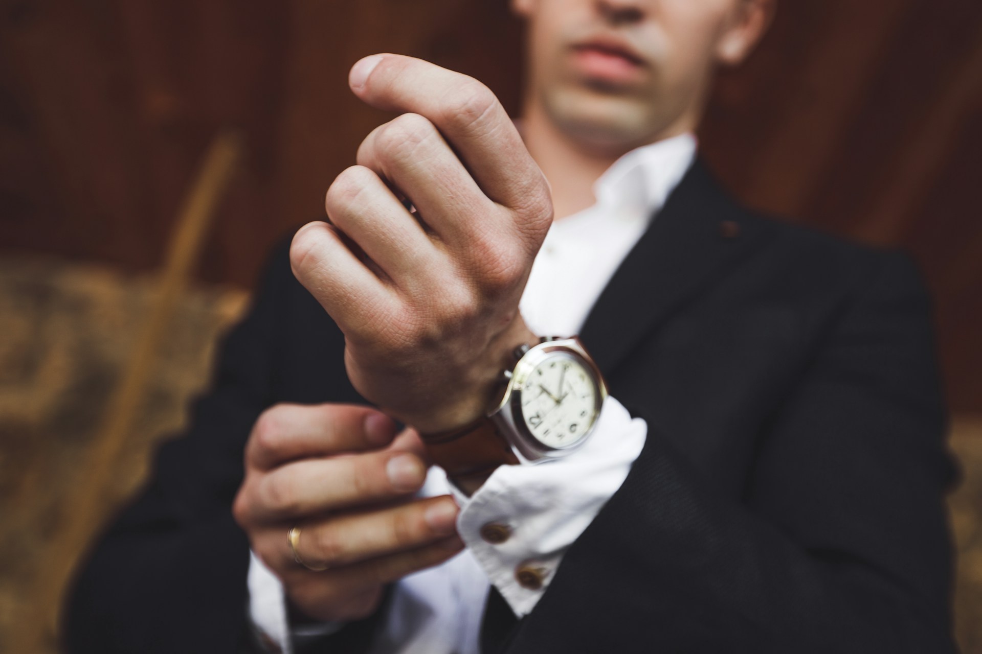 A close-up of a man putting a dress watch with a leather strap on his wrist.