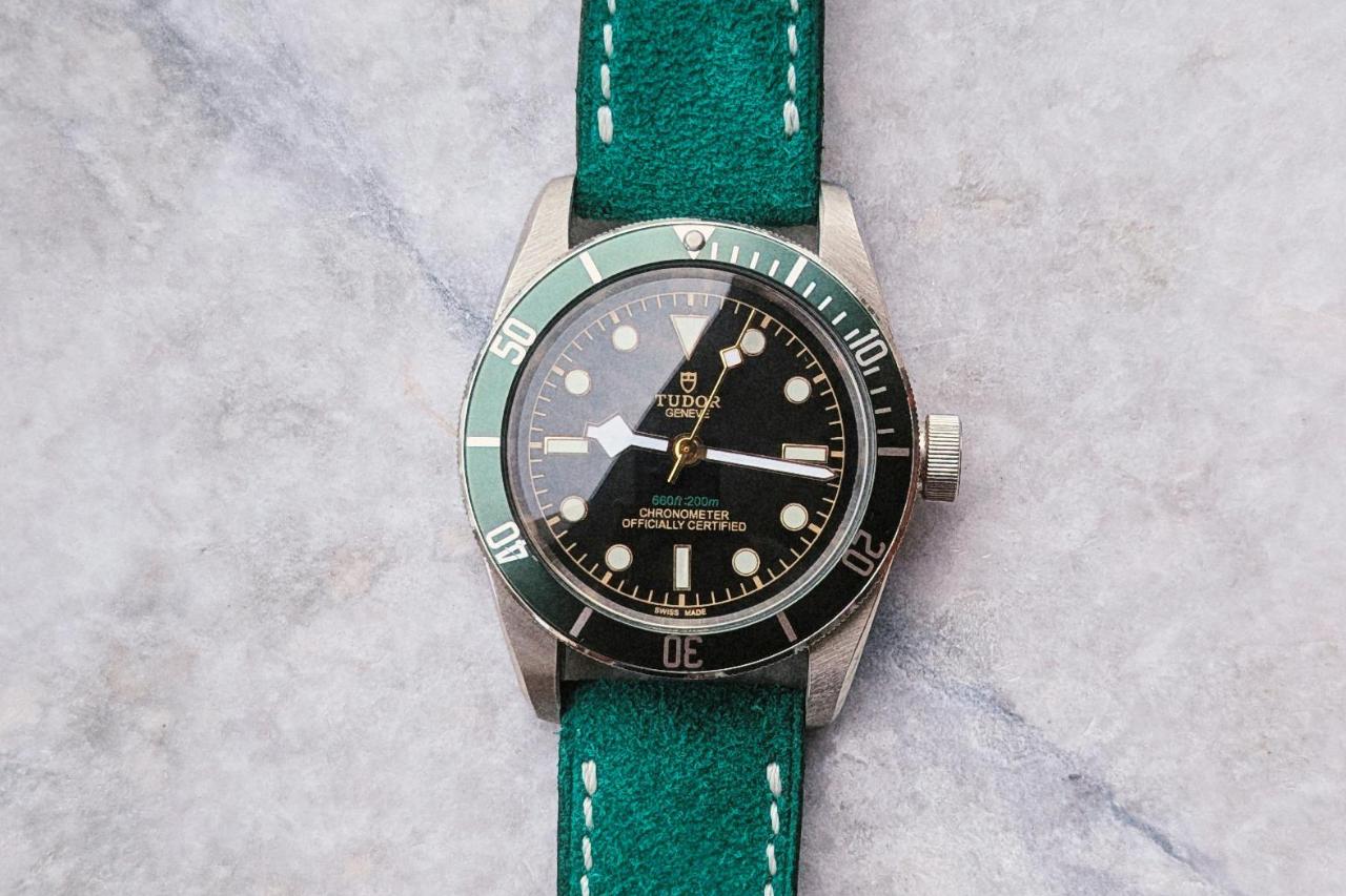 A TUDOR watch with a green bezel and black dial featuring gold markers and hands.