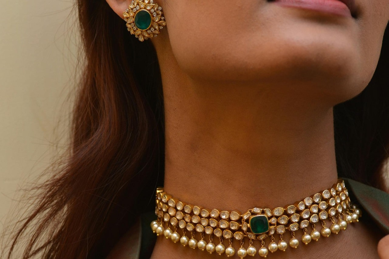 a woman wearing a matching earring and necklace set featuring emeralds, diamonds, and yellow gold