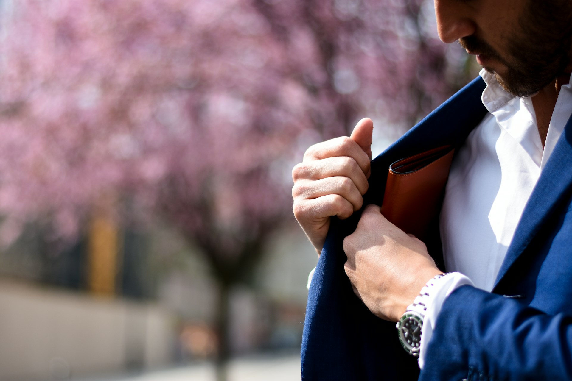 A man putting something in his coat pocket while wearing a luxury watch.