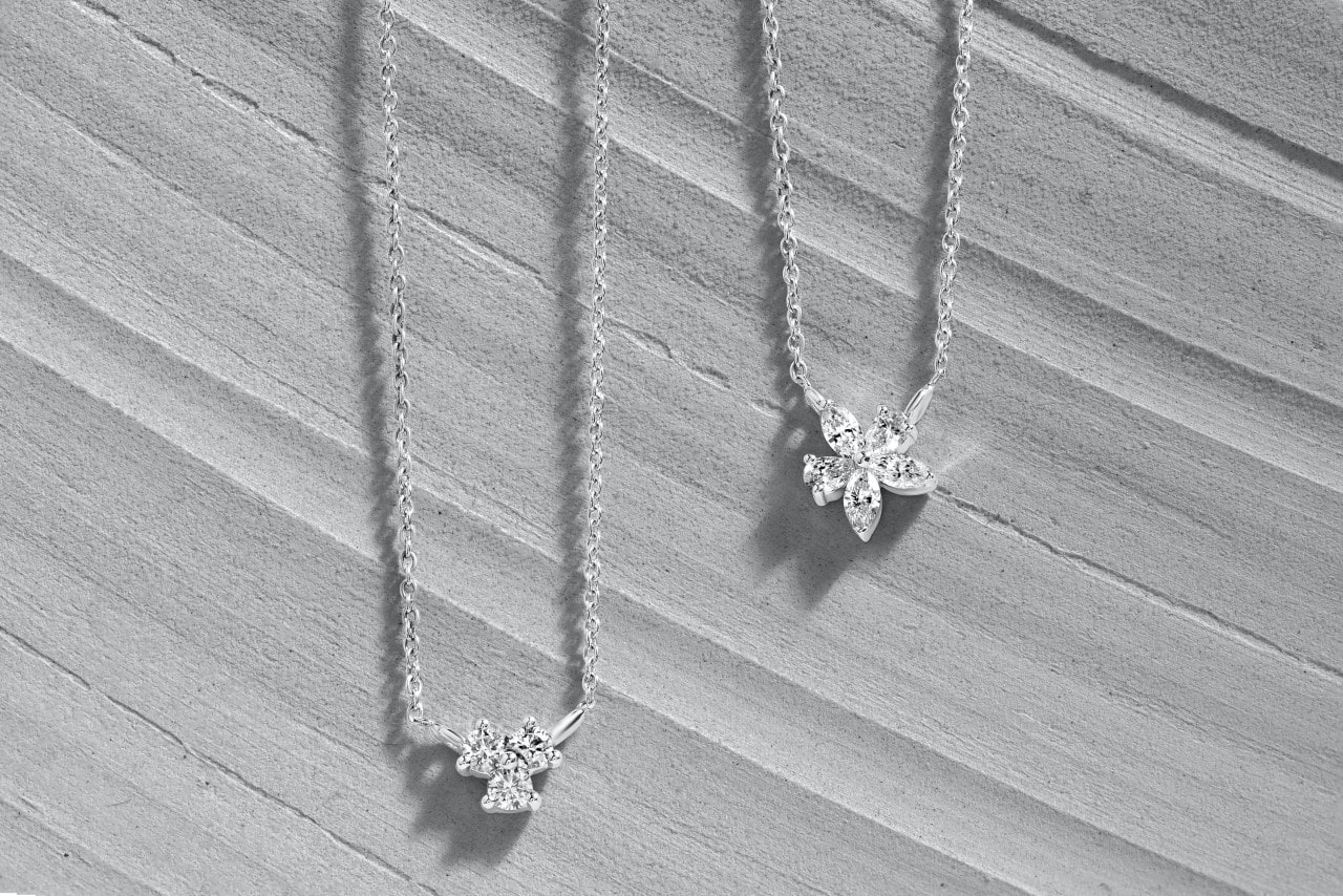 Two diamond-adorned white gold pendants sit on gray wood. Two diamond-adorned white gold pendants sit on gray wood.