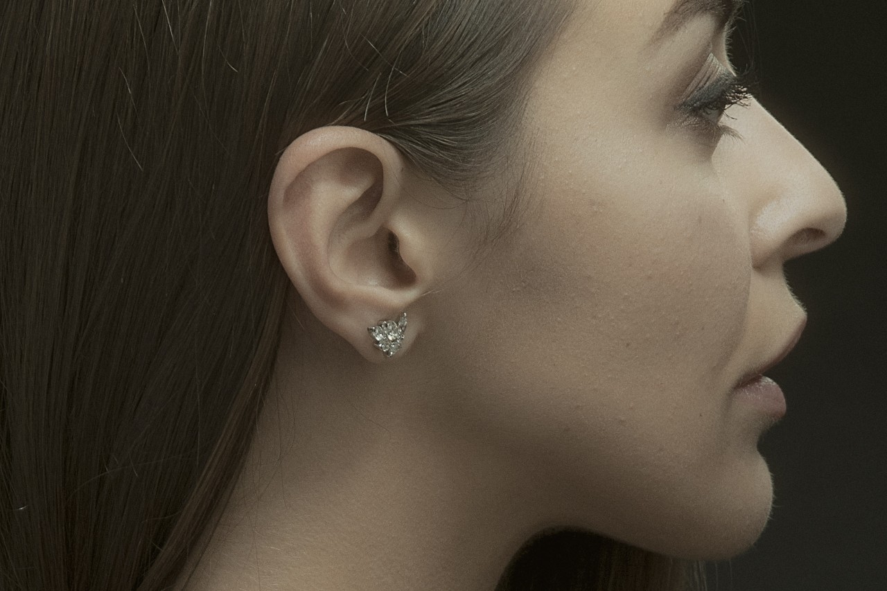 A woman looking off in the distance, wearing elaborate diamond stud earrings.