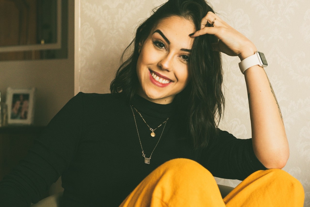 A woman sitting wears a smartwatch and two Van Cleef and Arpels necklaces. A woman sitting wears a smartwatch and two Van Cleef and Arpels necklaces.
