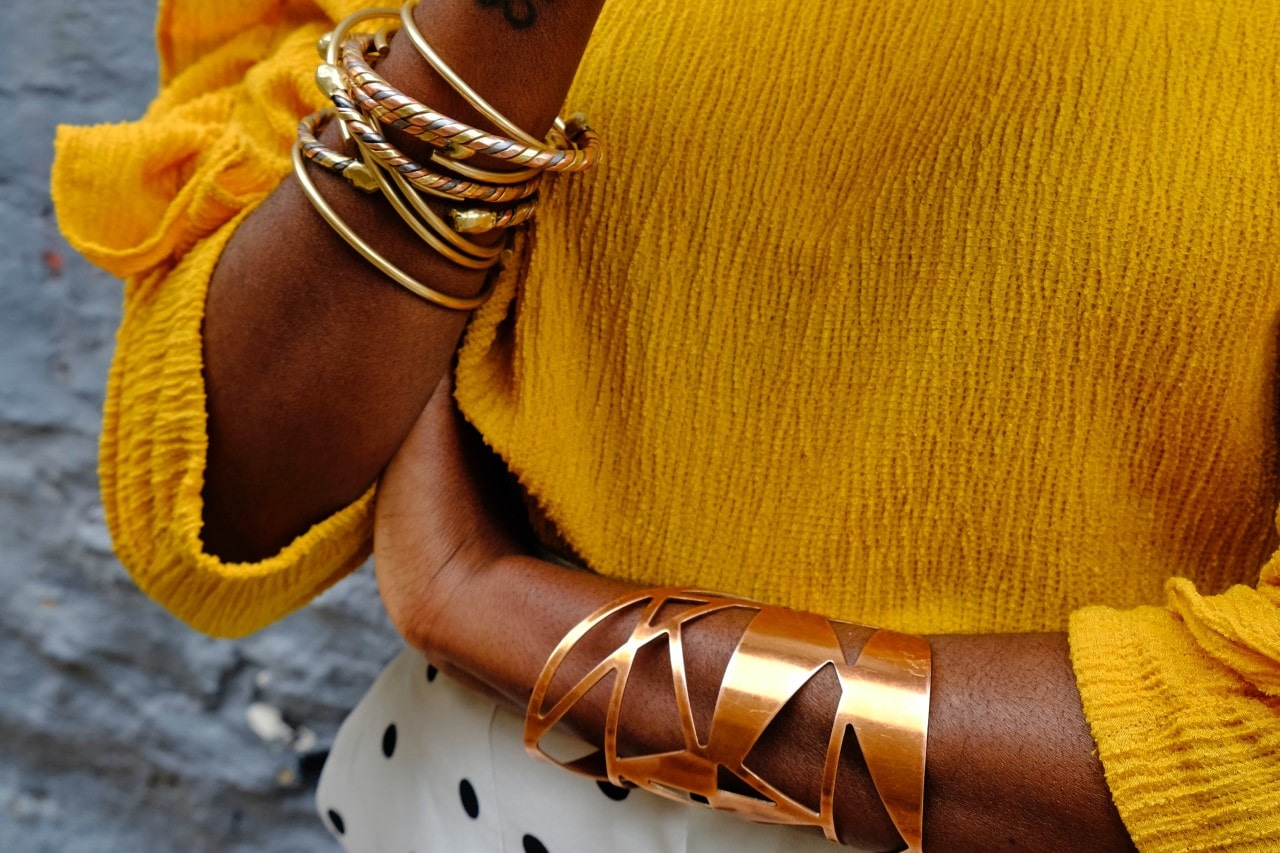 close up image of a woman’s arms wearing gold bangles and cuff bracelet