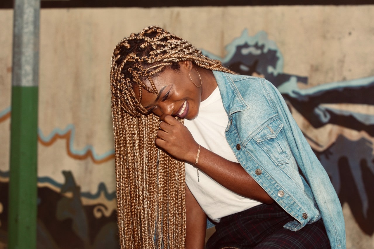 a woman bent over smiling and wearing gold jewelry and a denim jacket