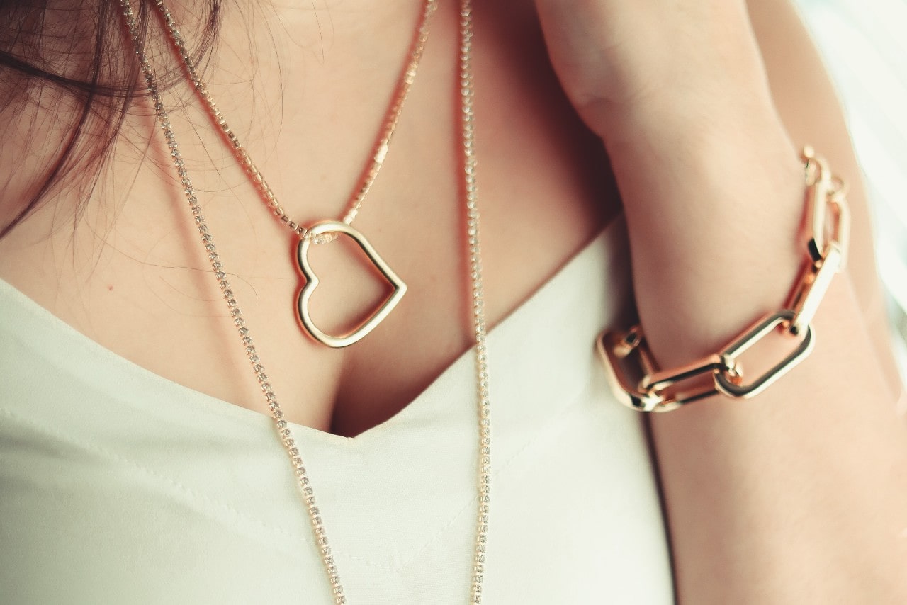 close up image of a woman wearing a chunky gold chain bracelet and heart necklaces