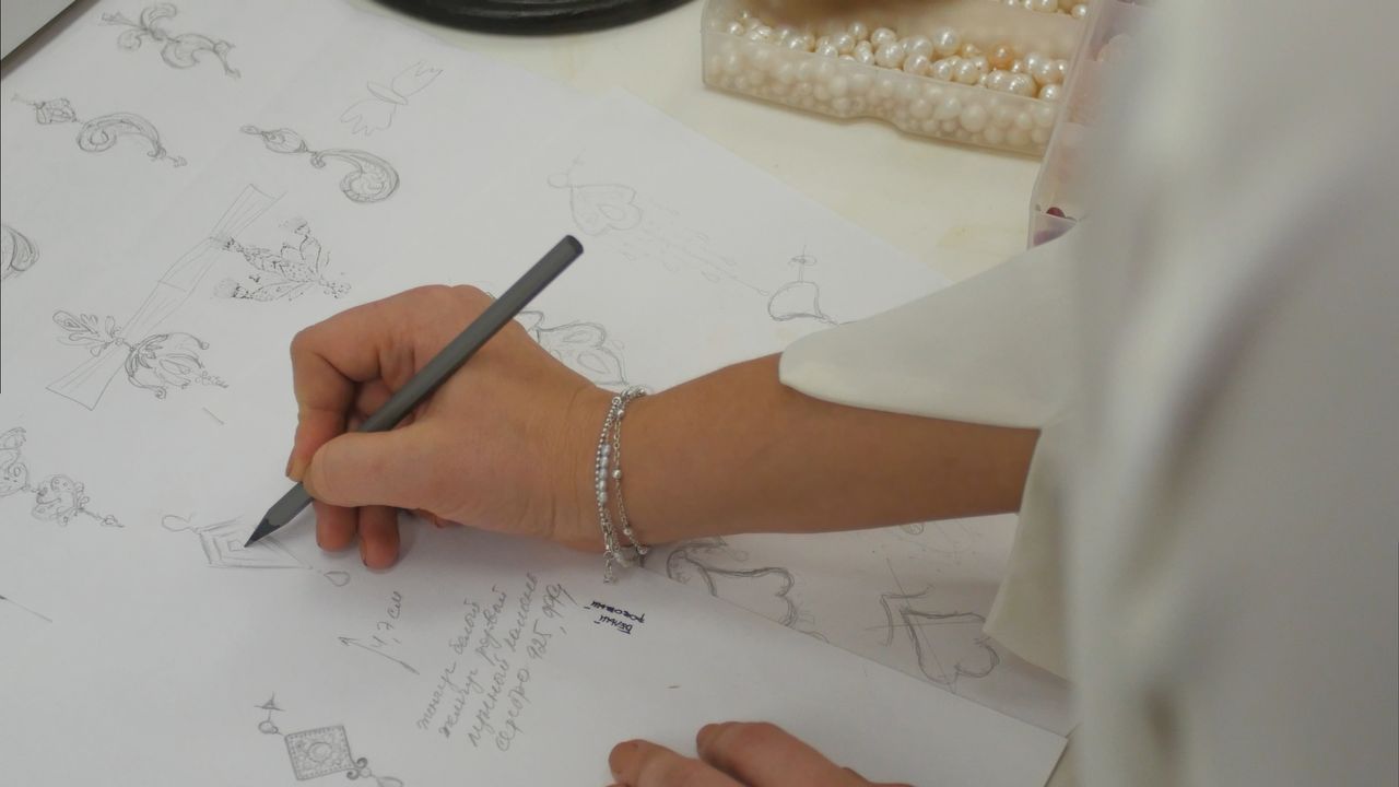 Close up of a jeweler sketching intricate jewelry designs with a pencil on paper. Close up of a jeweler sketching intricate jewelry designs with a pencil on paper.