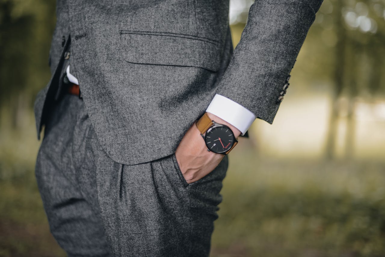 A person wearing a brown leather strap watch in a grey suit stands outdoors with one hand in their pocket. A person wearing a brown leather strap watch in a grey suit stands outdoors with one hand in their pocket.