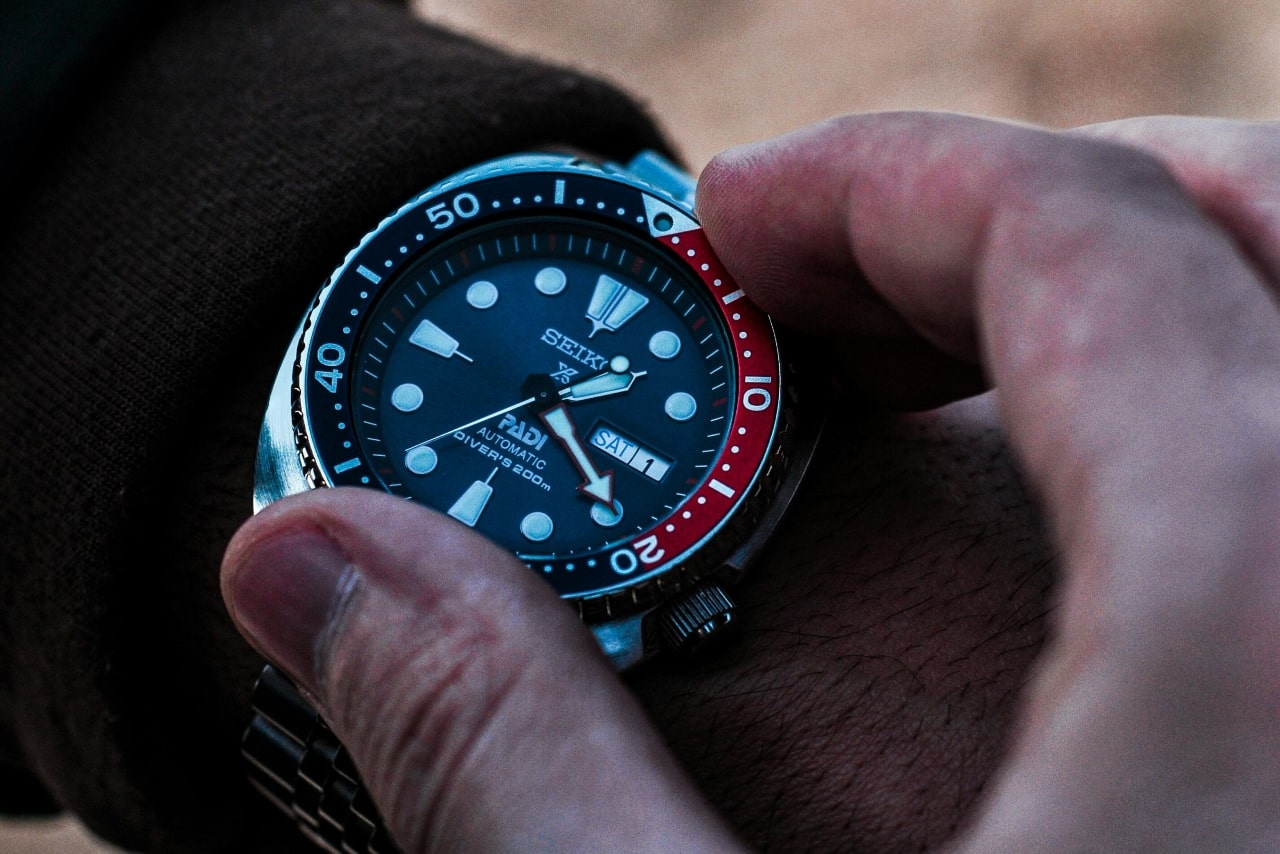 Close-up of a person’s hand adjusting wristwatch with a blue and red bezel. Close-up of a person’s hand adjusting wristwatch with a blue and red bezel.