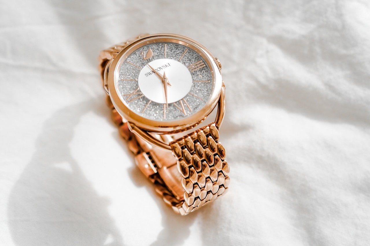 A gold wristwatch with a glittery silver face and Roman numerals rests on a white fabric. A gold wristwatch with a glittery silver face and Roman numerals rests on a white fabric.