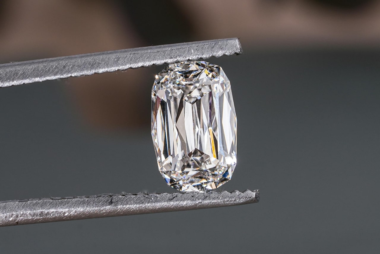 A close-up of a radiant diamont held carefully in a pair of jeweler’s tweezers.