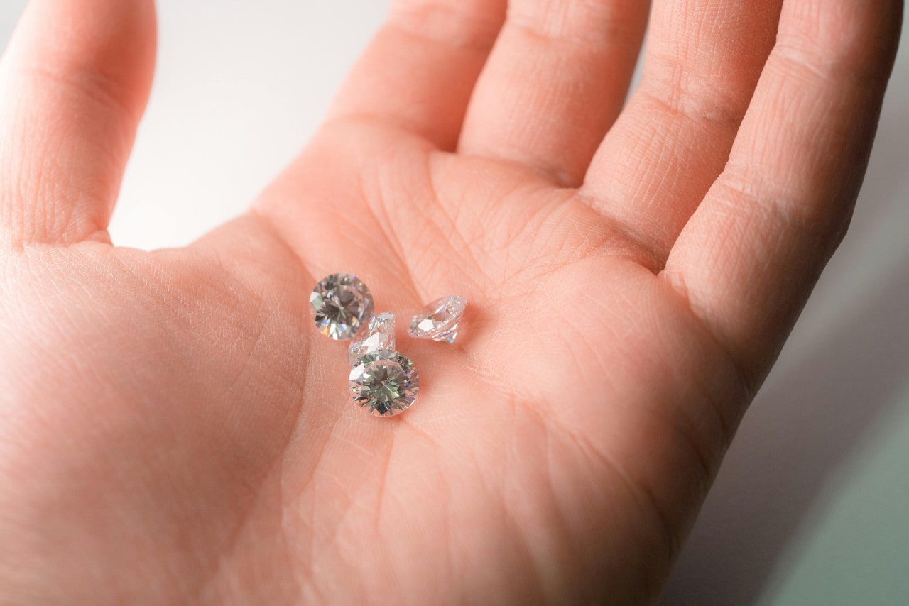 A close-up of four glistening round cut diamonds in the palm of a person’s hand.
