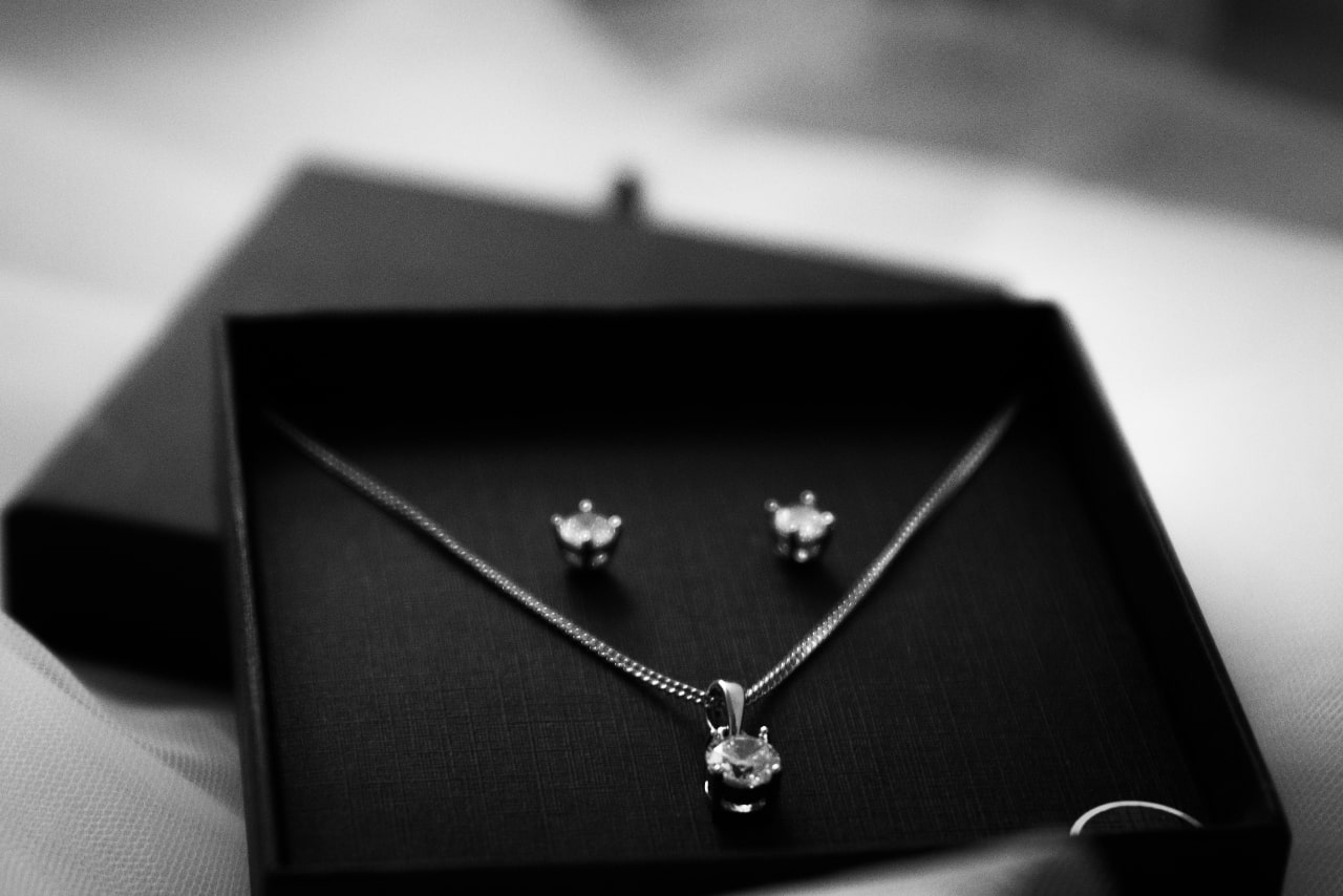 A black and white close-up of a matching jewelry set featuring a diamond pendant necklace and stud earrings.