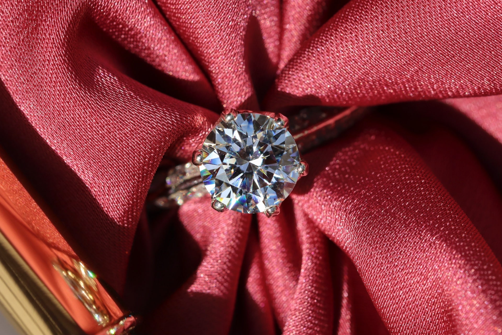 A close-up of a stunning solitaire diamond ring displayed on textured red fabric.
