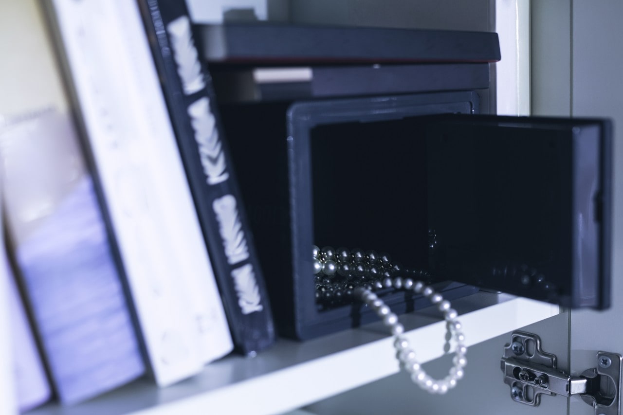 A close-up of a jewelry case on a bookshelf, with two strings of pearls visible through the open front. A close-up of a jewelry case on a bookshelf, with two strings of pearls visible through the open front.