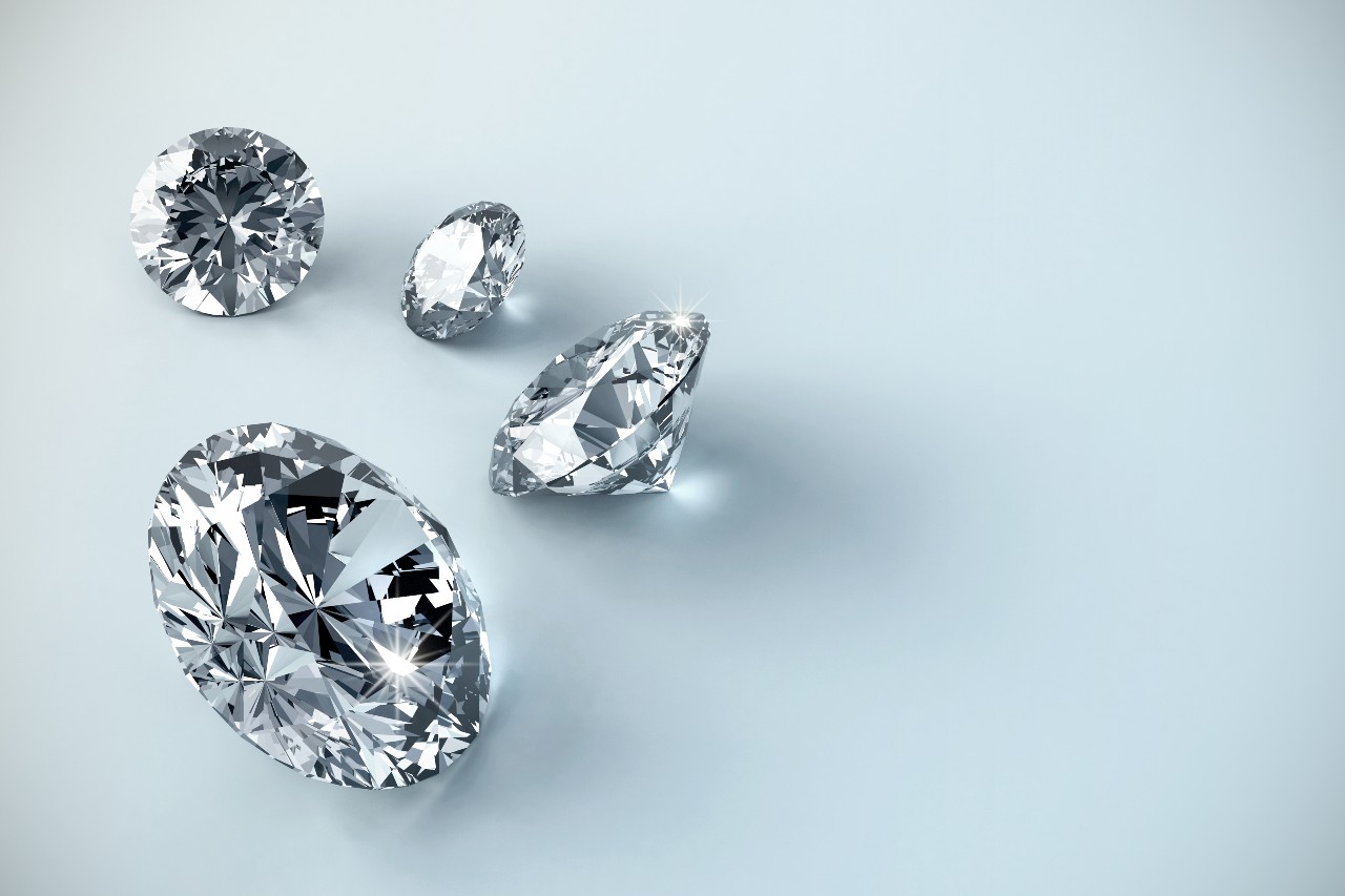A close up of four shiny diamonds on the left side of the photo, atop a light blue background.