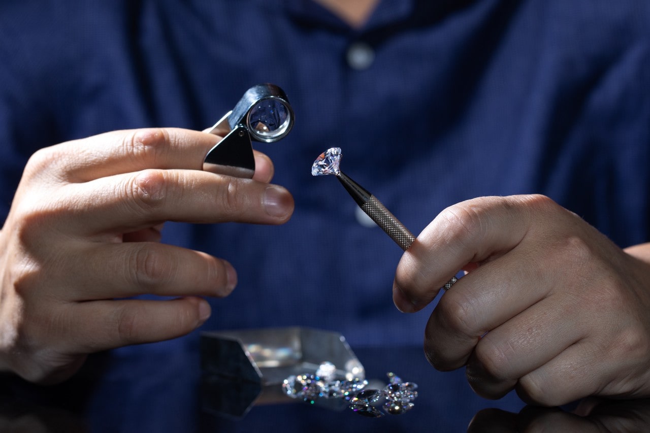 An expert jeweler in a navy blue shirt examining a diamond with a hand-held microscope.