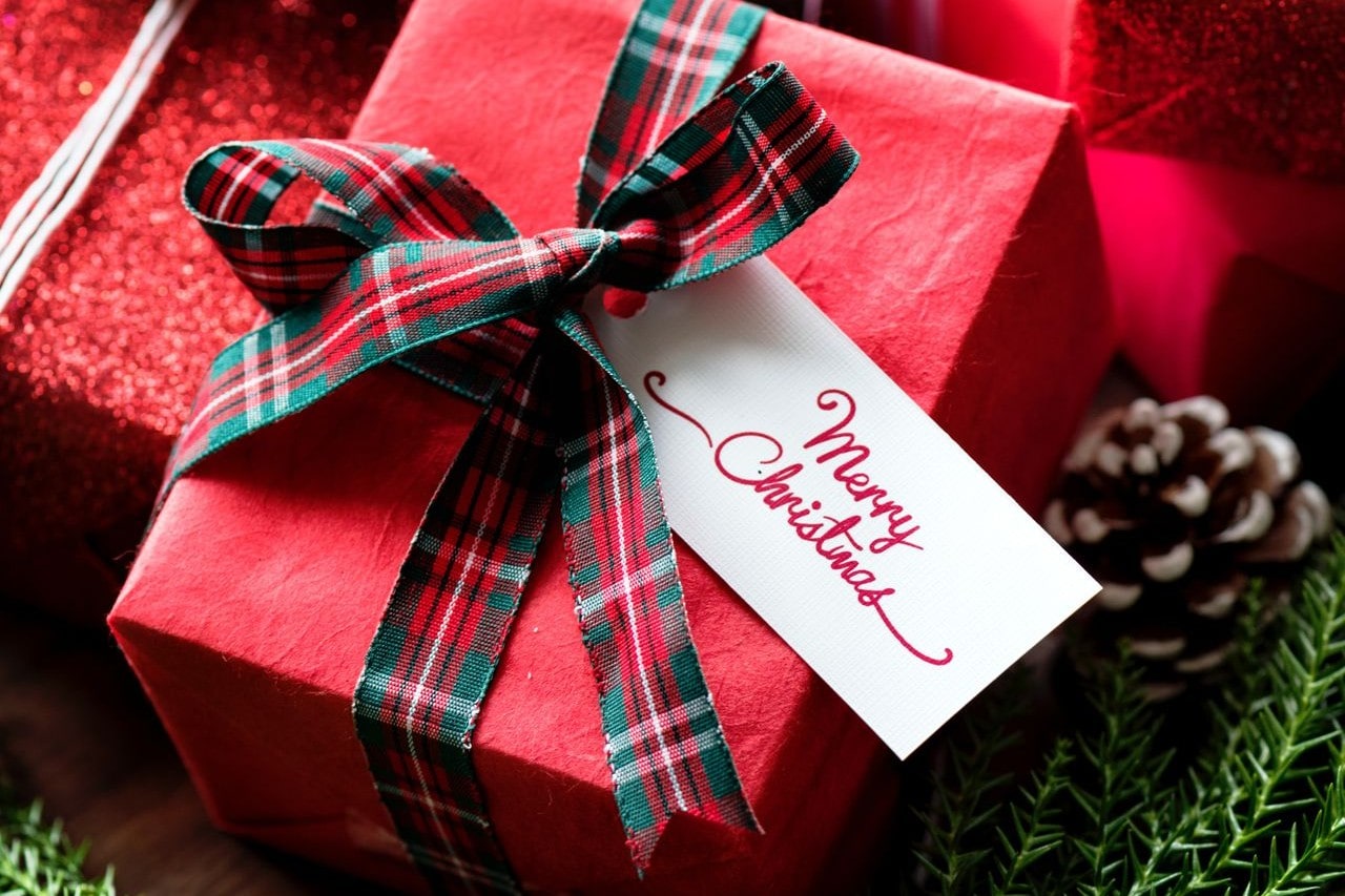 A close-up of a charming red gift box wrapped in red paper and tied with a plaid ribbon, the tag reading “Merry Christmas.”