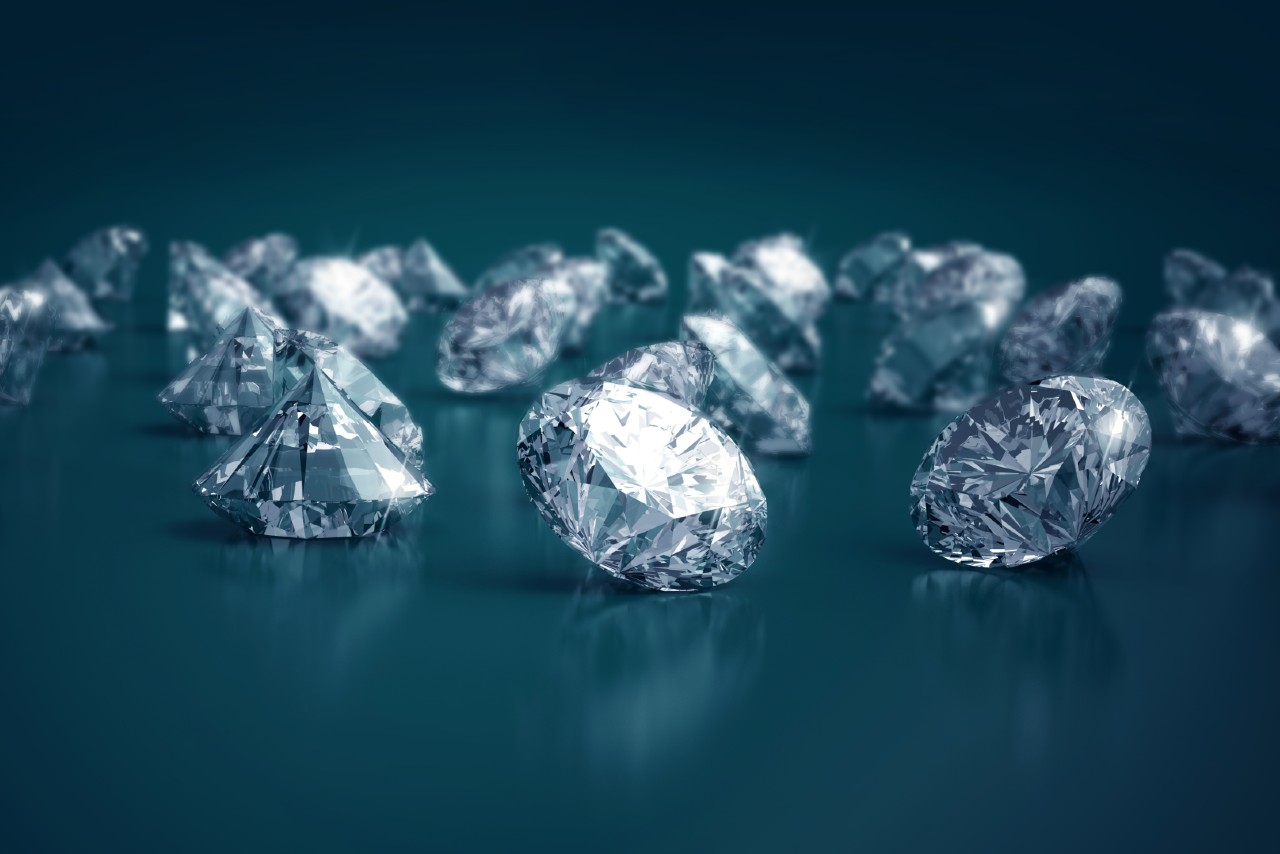 A close-up of multiple stunning round-cut diamonds on a reflective dark teal surface.