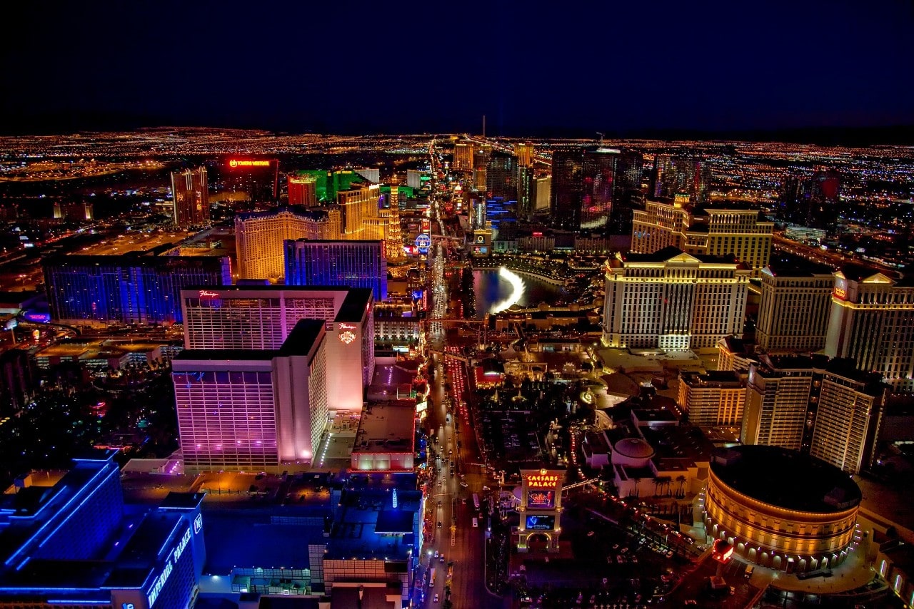 A vibrant nighttime aerial view of the Las Vegas strip, brilliantly lit by the hotels and casinos along the road.