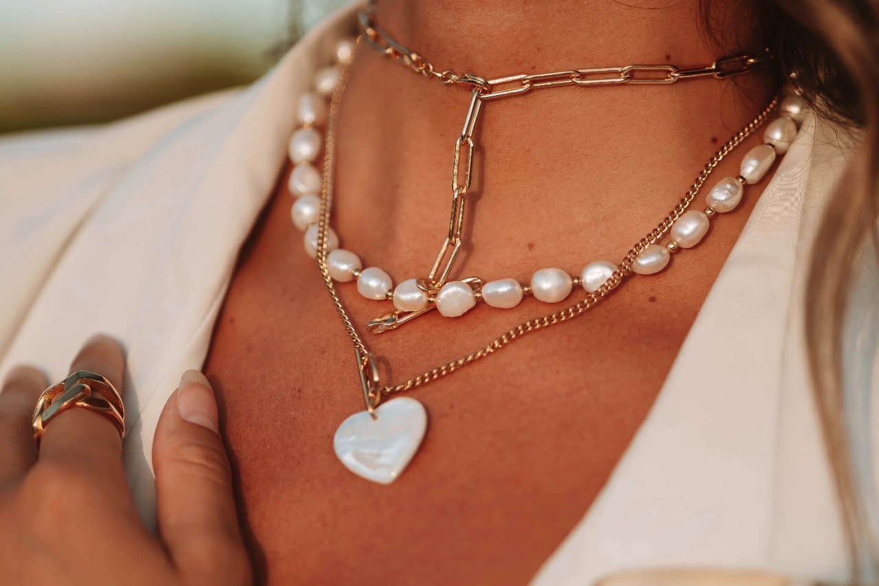 A close-up of a fashionable woman wearing three distinctive layered necklaces with a white jacket. A close-up of a fashionable woman wearing three distinctive layered necklaces with a white jacket.