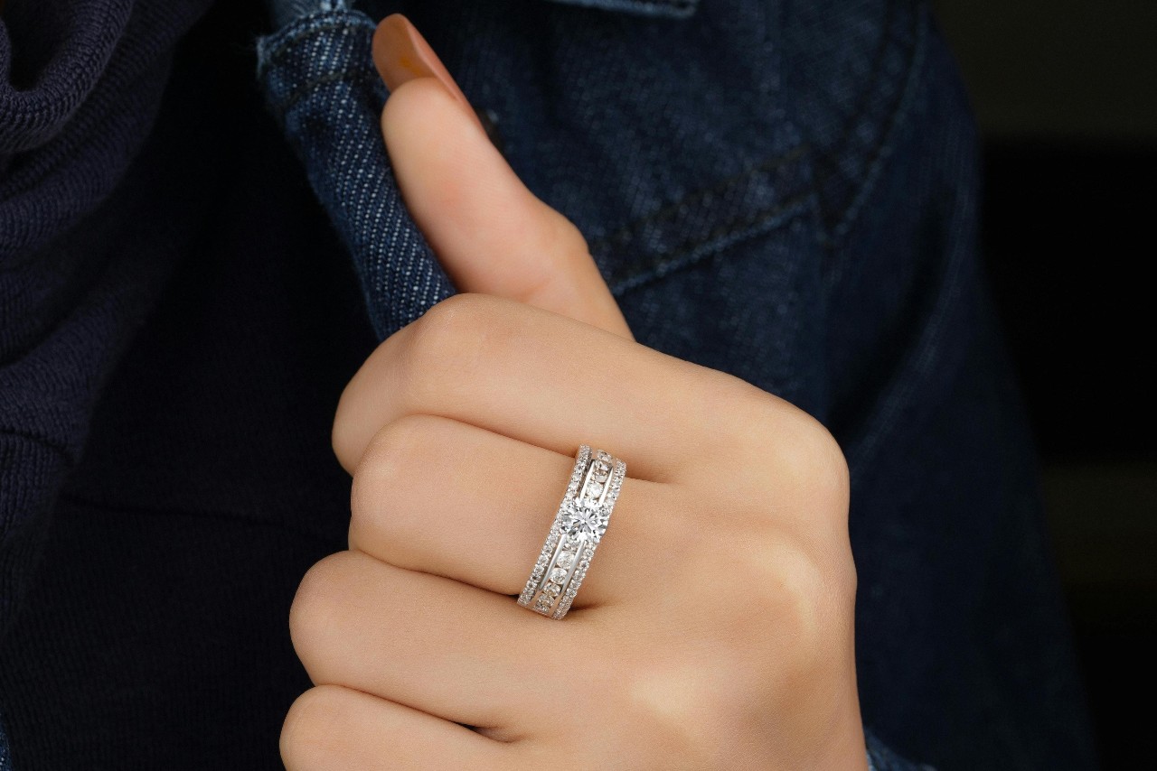 A close-up of a woman’s hand holding the front of her denim jacket, with emphasis on the dazzling white gold diamond ring on her finger.
