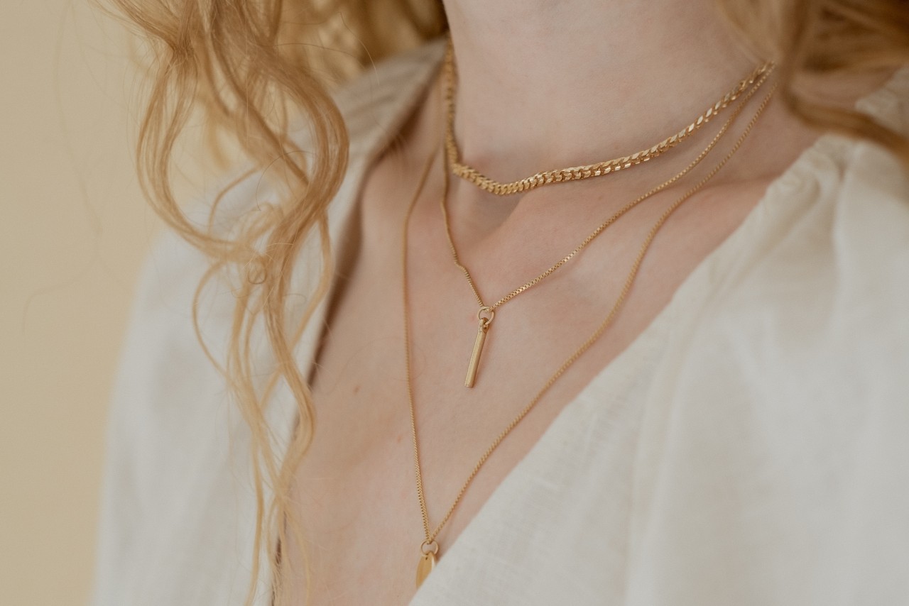 A close-up of a woman’s neck and decolletage, adorned with delicate layers of yellow gold necklaces.