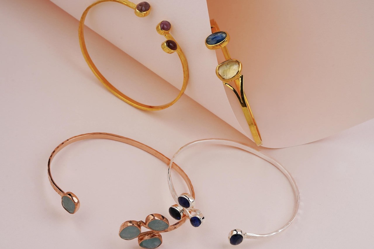 A close-up of four gold and gemstone bangle bracelets, two crafted from yellow gold, and one each crafted from rose gold and white gold.