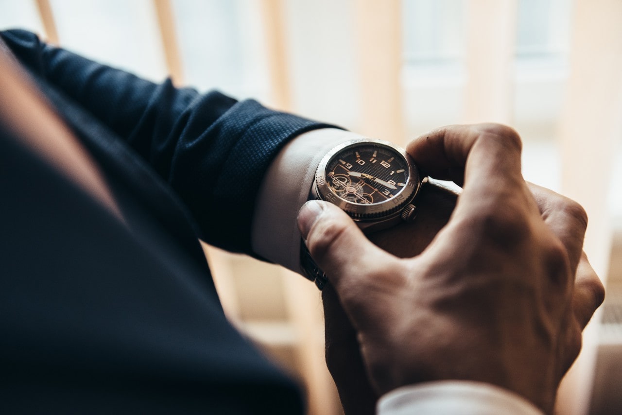 Close-up of a person in a dark blue suit adjusting a wristwatch in a dimly lit setting. Close-up of a person in a dark blue suit adjusting a wristwatch in a dimly lit setting.