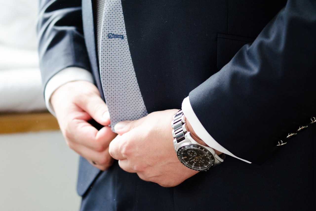 A man in a dark blue suit fixes his shirt, while showcasing a stainless steel watch with black dial and contrasting hands. A man in a dark blue suit fixes his shirt, while showcasing a stainless steel watch with black dial and contrasting hands.