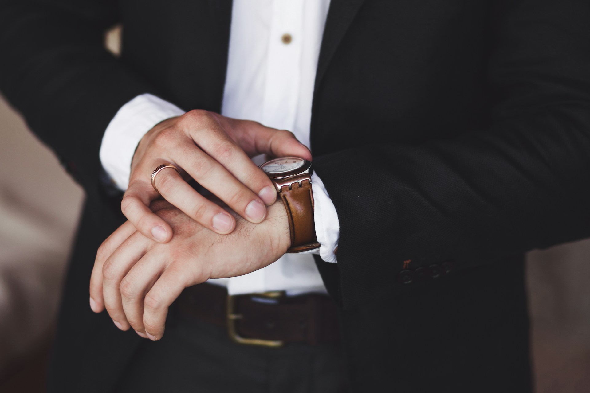 A close up of a man in the black suit fixing his brown leather wristwatch with white dial